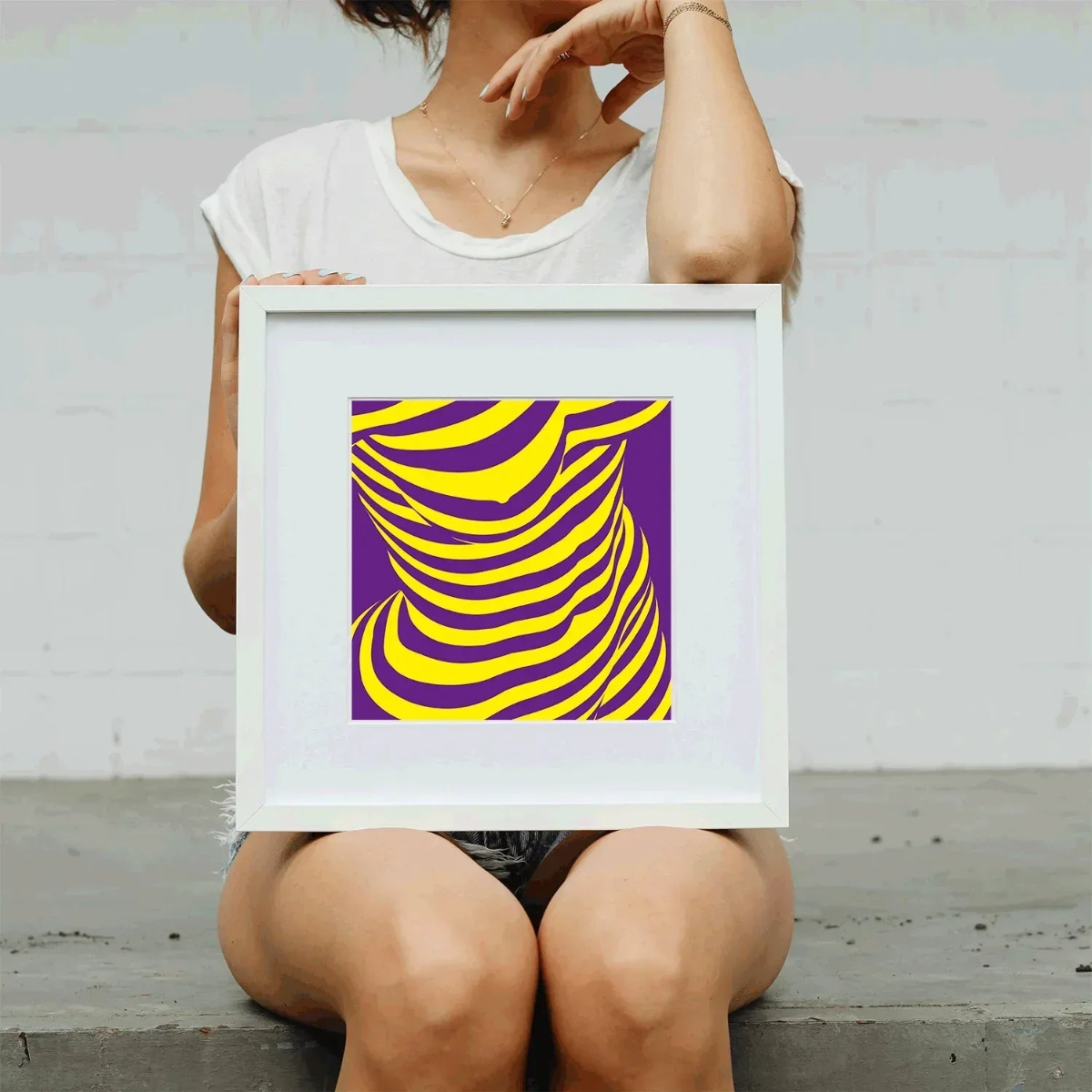 Person holding a framed abstract art print with purple and yellow design.