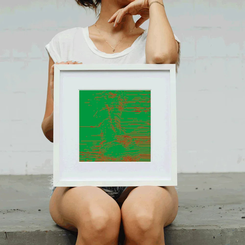 Person holding a framed abstract artwork with green and red patterns against a plain background