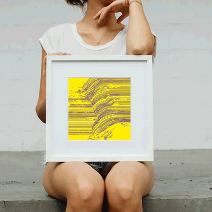 Person holding a framed yellow and purple abstract art print against a plain background