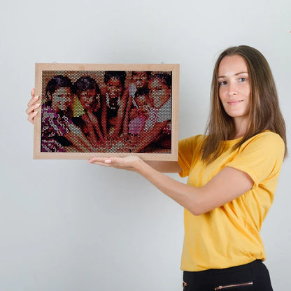 Woman holding a framed mosaic artwork of a group of people against a plain background